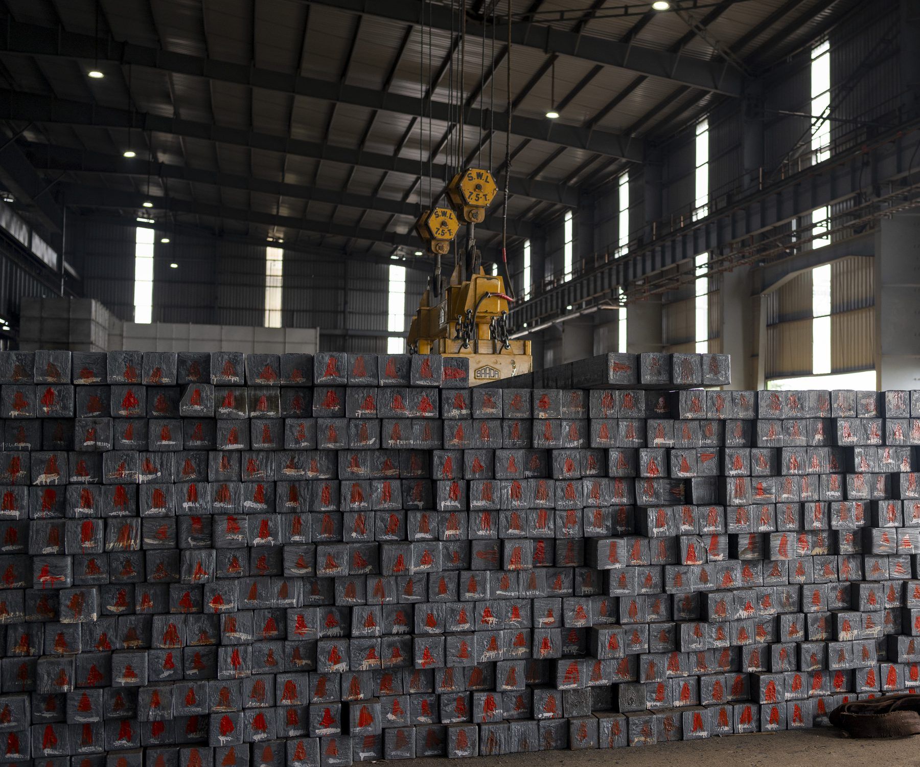 Stacked steel billets marked in red paint under a magnetic crane